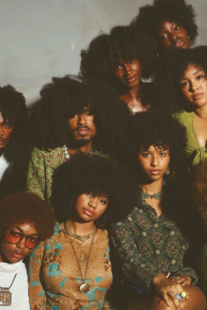 A group of diverse individuals with natural, voluminous hairstyles, posing closely together in a stylish arrangement. They are wearing vibrant, retro clothing that reflects a nostalgic aesthetic.